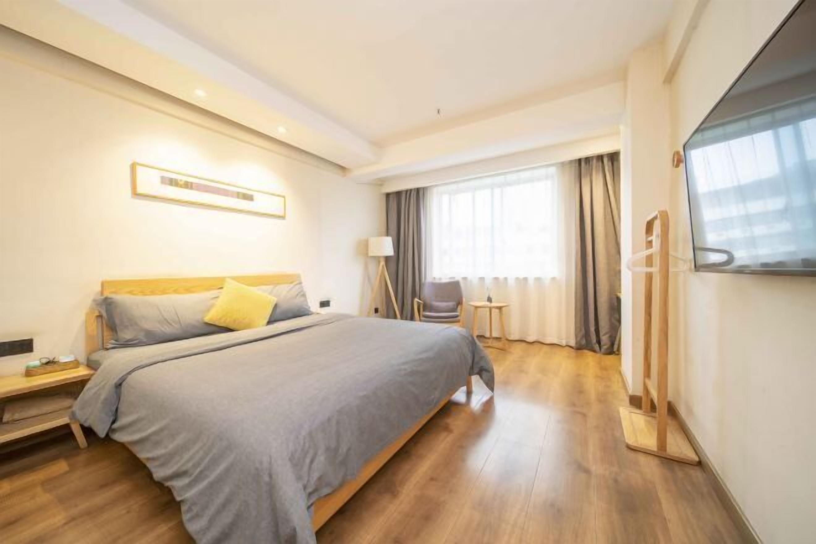 A hotel room with a large bed, a bedside table, a TV, and a window with curtains.