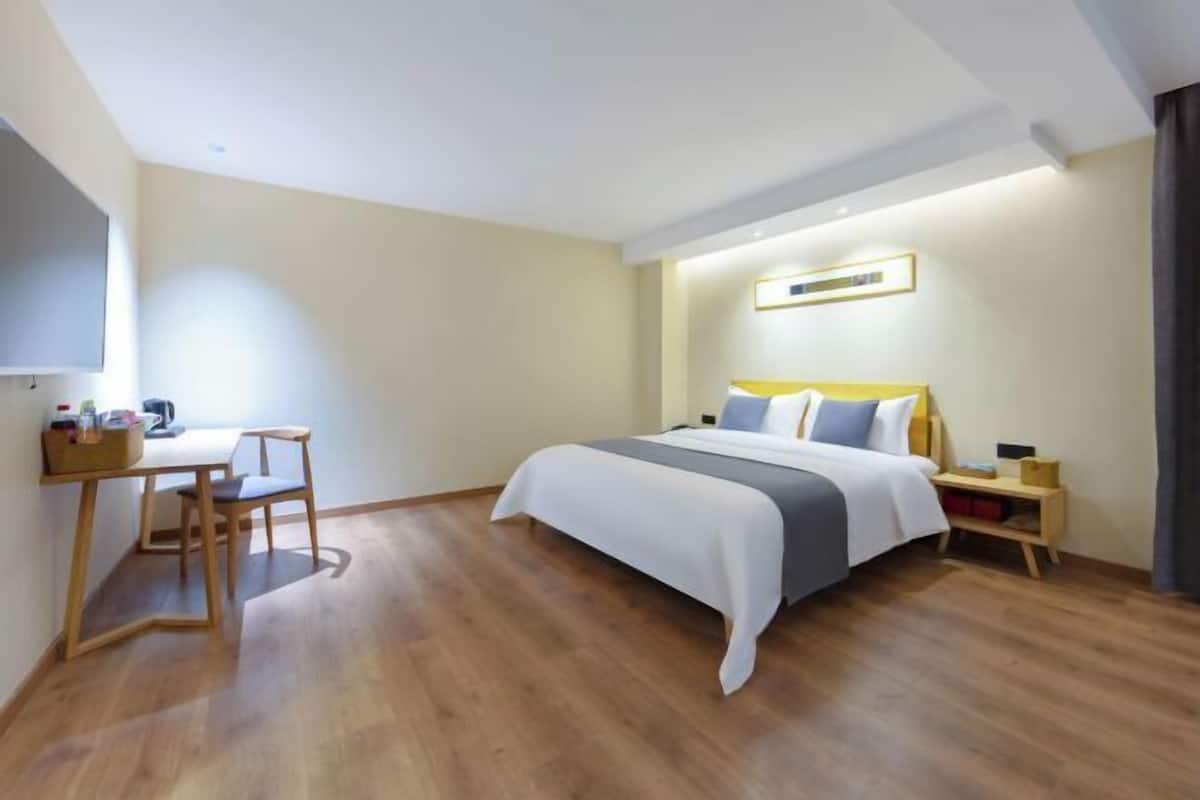 A bedroom with a bed, bedside table, chair, desk, and a small shelf.
