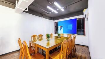 A conference room with a glass table, wooden chairs, and a blue screen on the wall.