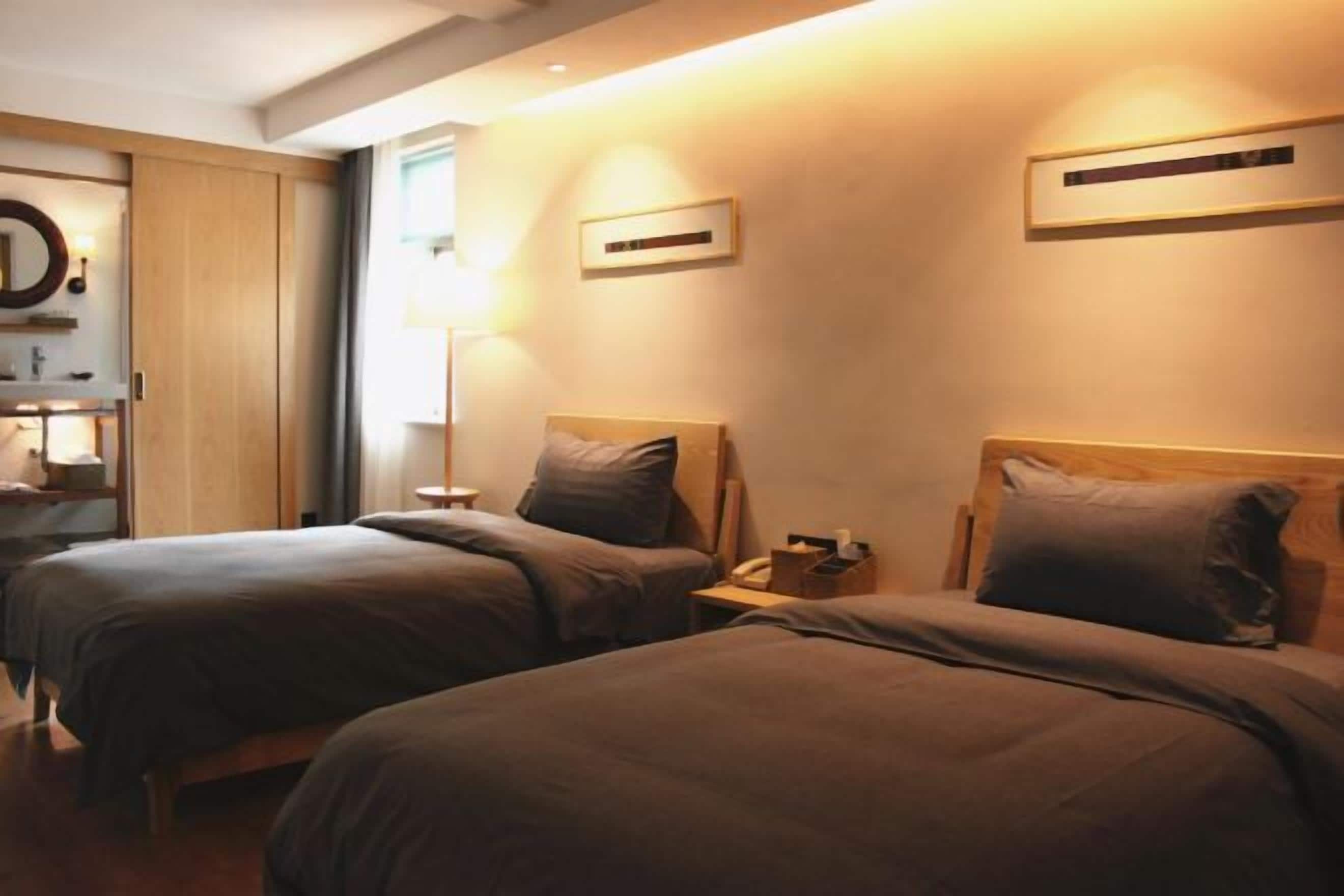 A hotel room with two beds, a bedside table with a lamp, and a wooden wardrobe.