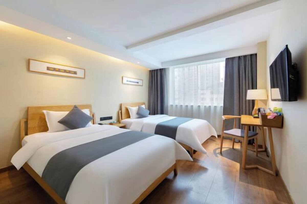 A hotel room with two beds, a desk, a chair, a TV, and a window with curtains.