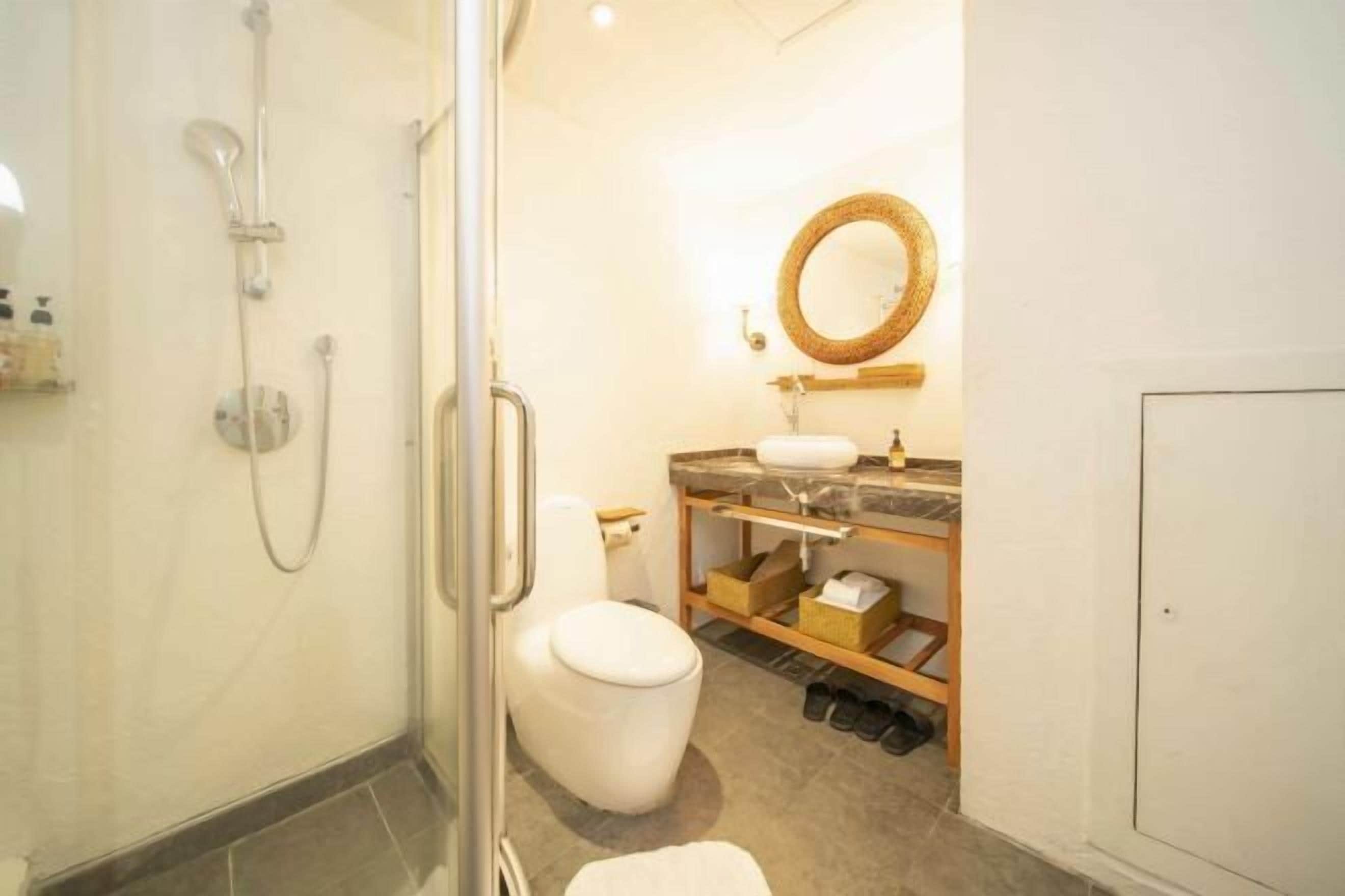 Een moderne badkamer met een douchecabine van glas, een wit toilet, een houten wastafelmeubel met spiegel en een opbergplank.