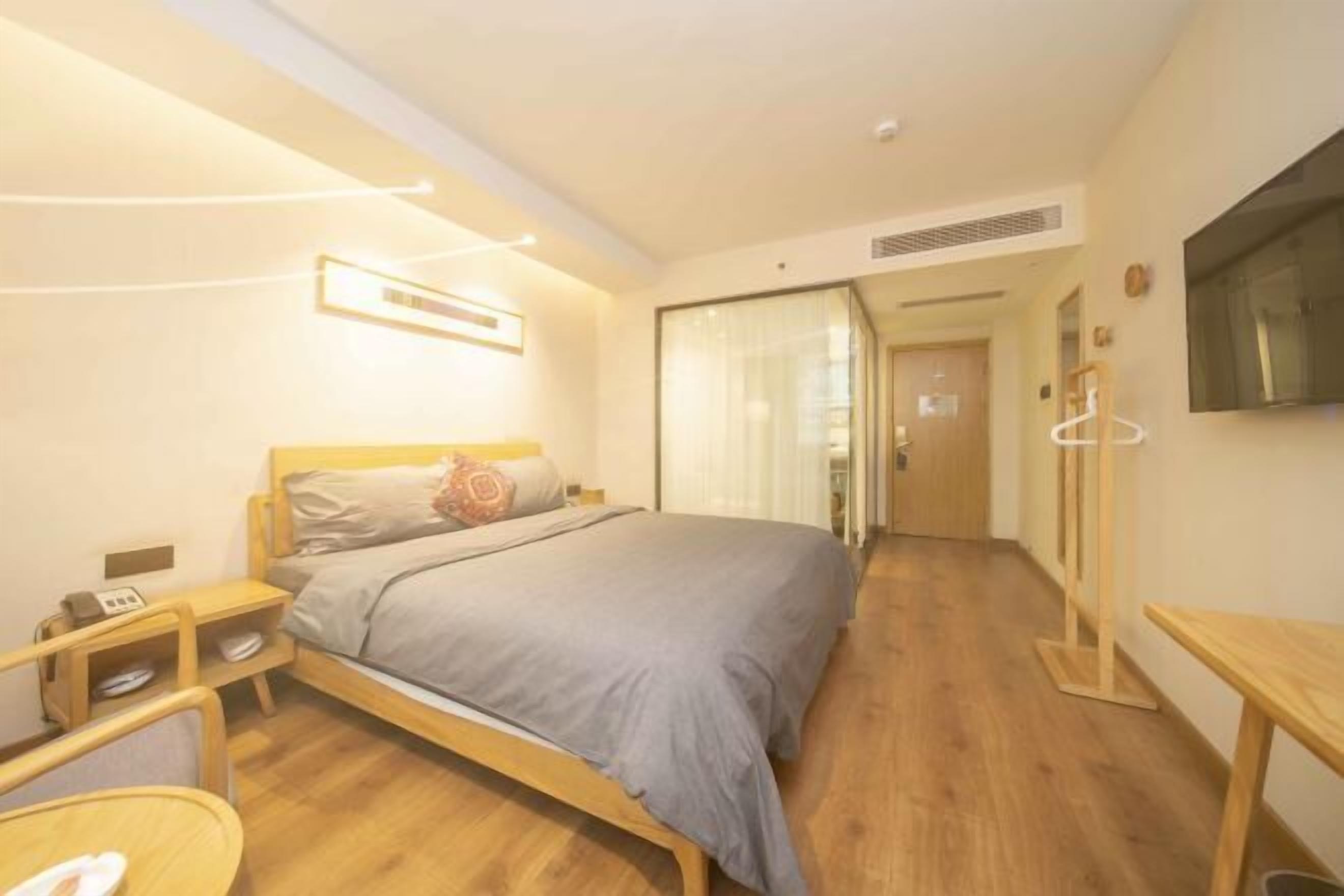A modern hotel room with a wooden bed, bedside tables, a TV mounted on the wall, and a wooden floor.