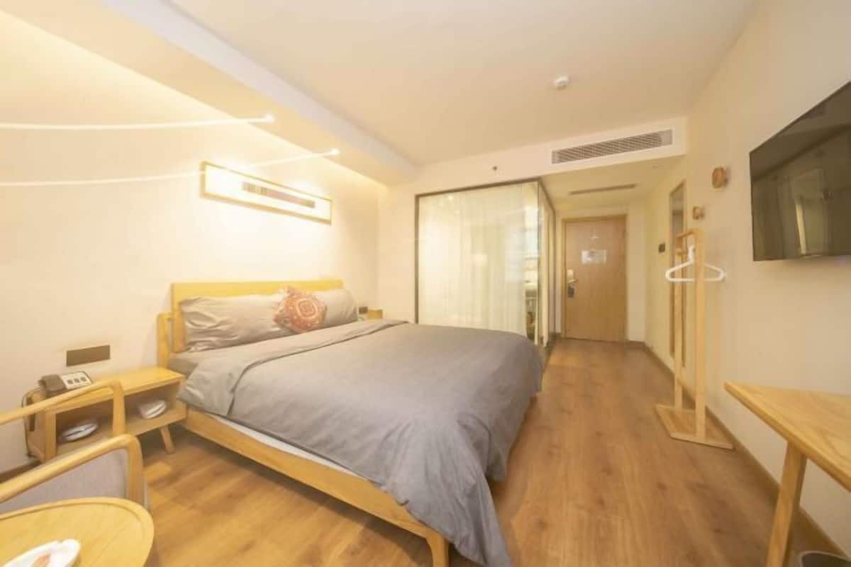 A modern hotel room with a wooden bed, bedside tables, a TV mounted on the wall, and a wooden floor.