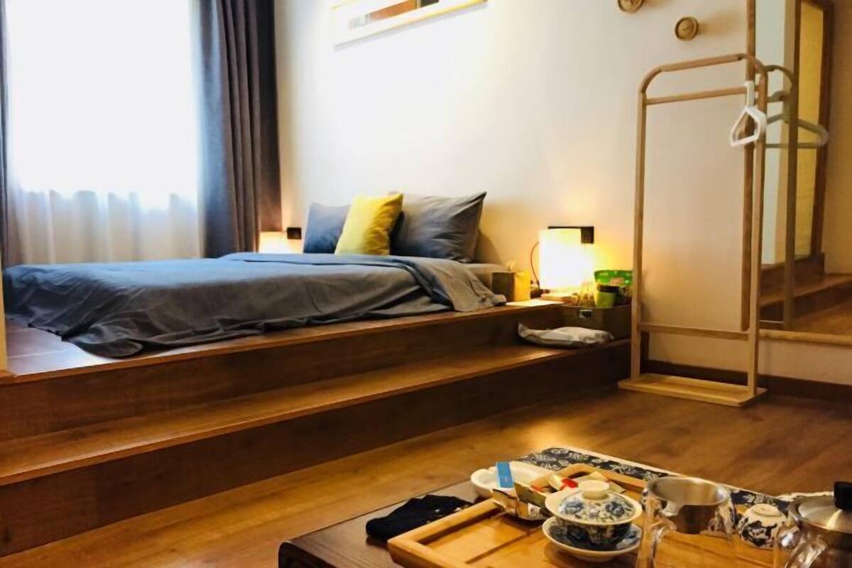 A hotel room with a bed, wooden steps, a table with tea set, and a mirror.