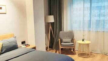Hotelkamer met een bed, een stoel, een tafeltje, een lamp en een raam met gordijnen.