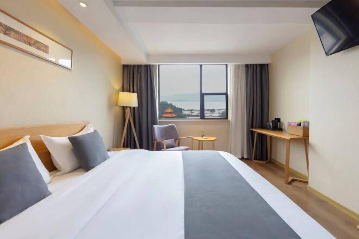 A hotel room with a bed, a desk, a chair, a TV, and a window with a view.