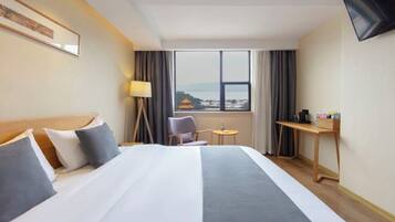 Habitación de hotel con cama, escritorio, silla, televisión y ventana con vistas.