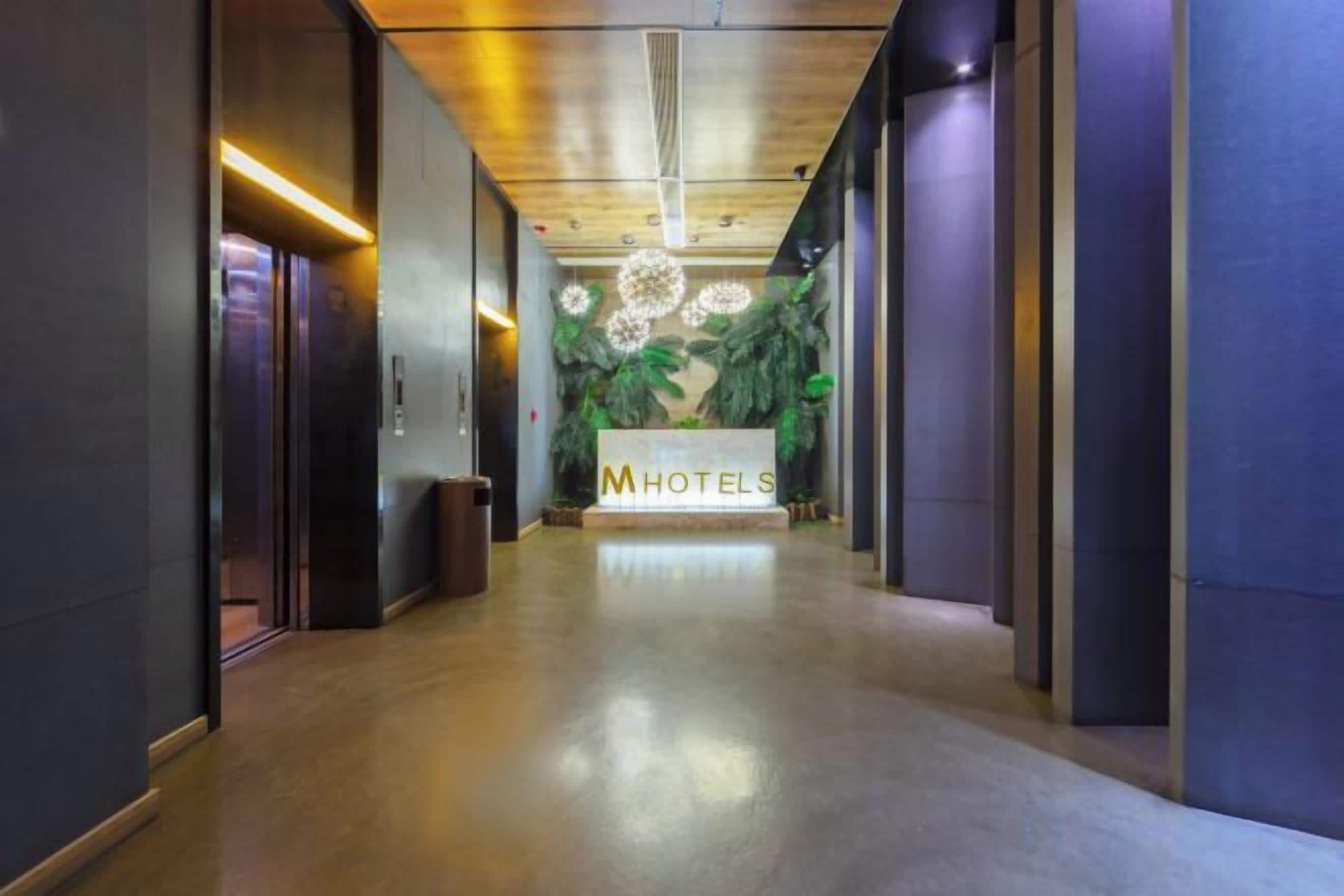 A hotel reception area with a reception desk, a trash bin, and a wall with a floral design.