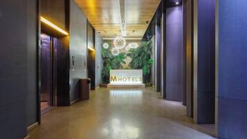 A hotel reception area with a reception desk, a trash bin, and a wall with a floral design.