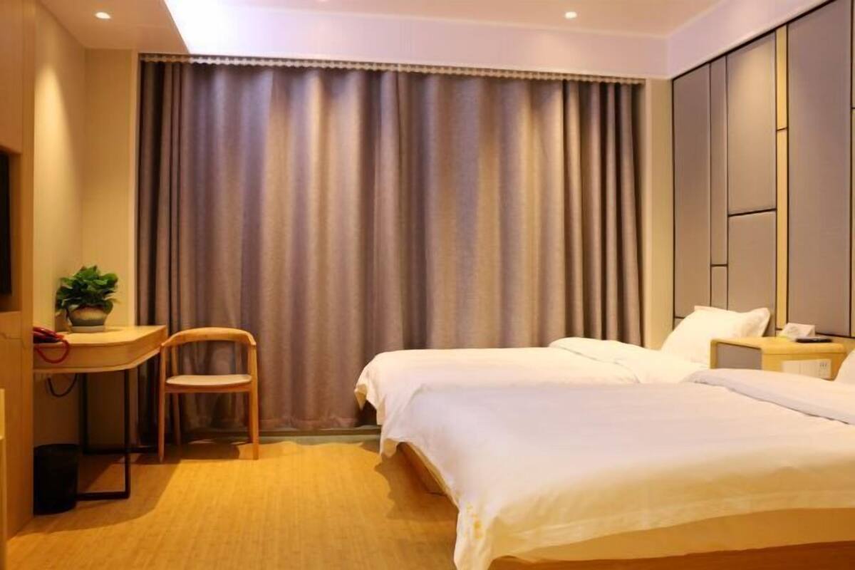 Habitación de hotel con dos camas, un escritorio con una silla, una planta en maceta y una cortina.
