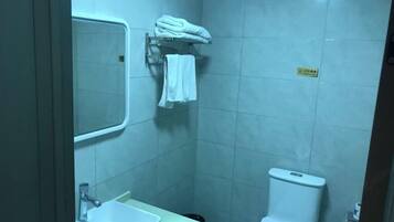 A small bathroom with a sink, a mirror, a toilet, and a towel rack with folded towels.