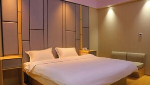 A hotel room with a large bed, a bedside table, a nightstand, and a seating area with a cushioned bench. - Huatian Hotel (Khorgas)