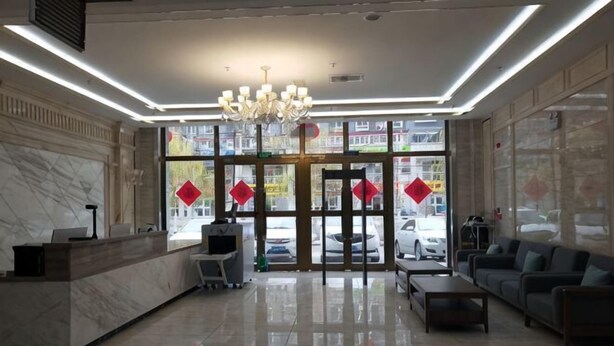 A hotel lobby with a reception desk, seating area, chandelier, and large windows. - Huatian Hotel (Khorgas)