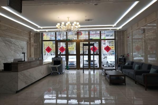 A hotel lobby with a reception desk, seating area, chandelier, and large windows. - Huatian Hotel (Khorgas)