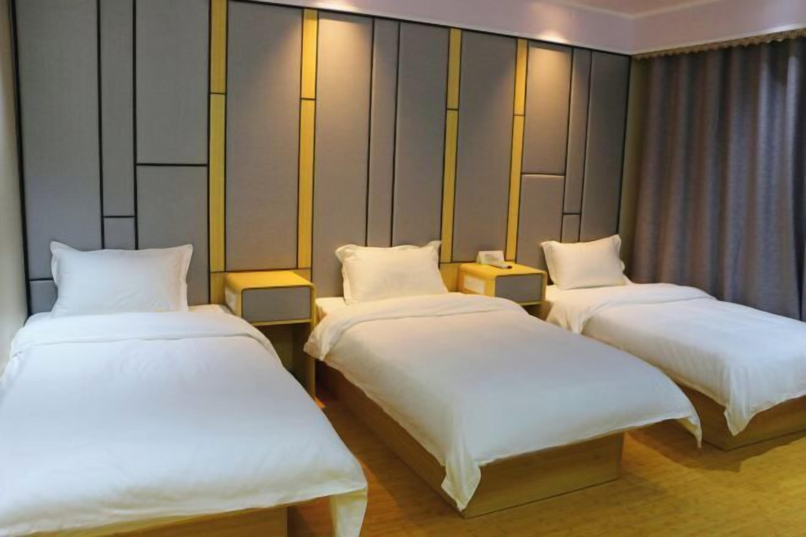 A hotel room with three single beds, each with a white bedspread and pillow, and a headboard with a geometric design.