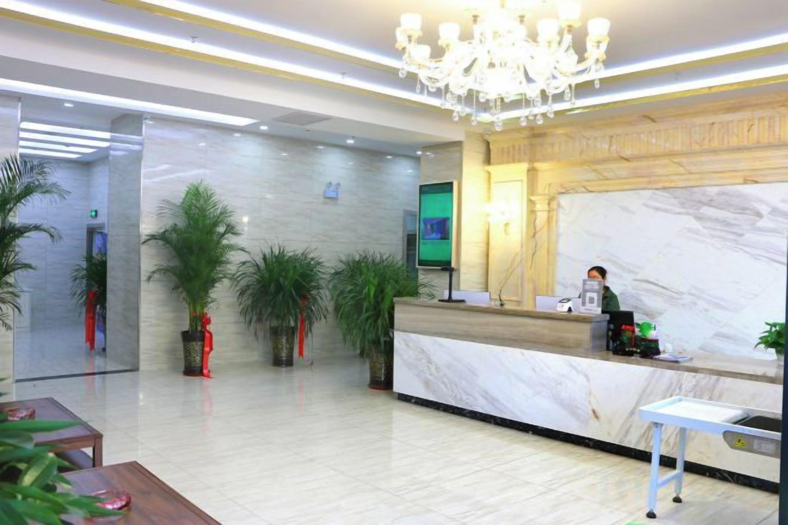 A hotel reception area with a marble counter, a chandelier, and potted plants.