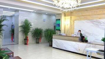 A hotel reception area with a marble counter, a chandelier, and potted plants.