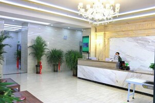 Una zona de recepción de hotel con mostrador de mármol, un candelabro y plantas en macetas.