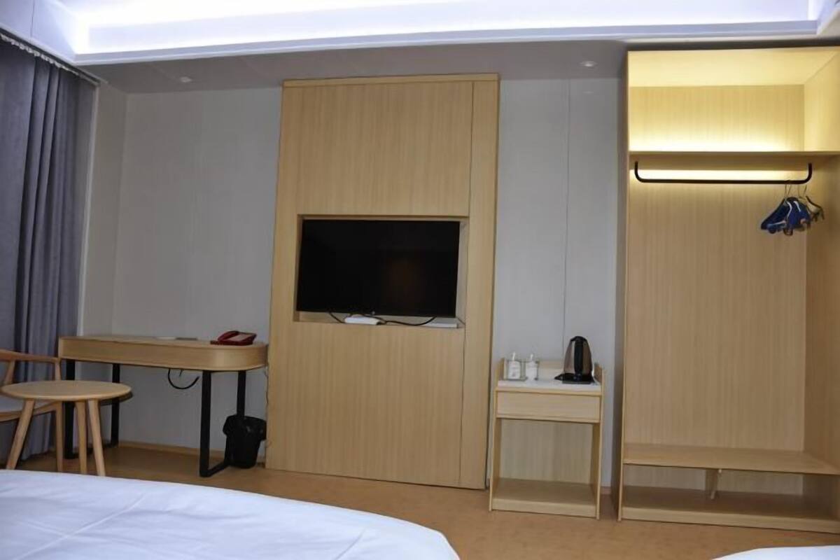 Habitación de hotel con cama, escritorio con televisor, mesita con tetera y armario.