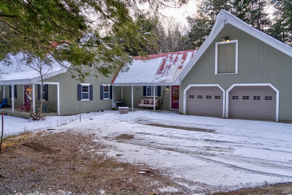 Two-story building with a gabled roof and covered porch area, featuring a garage with two doors and a small shed.