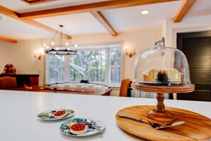 Enjoy meals in this stylish dining area with a wooden table, glass cake stand, and large window.