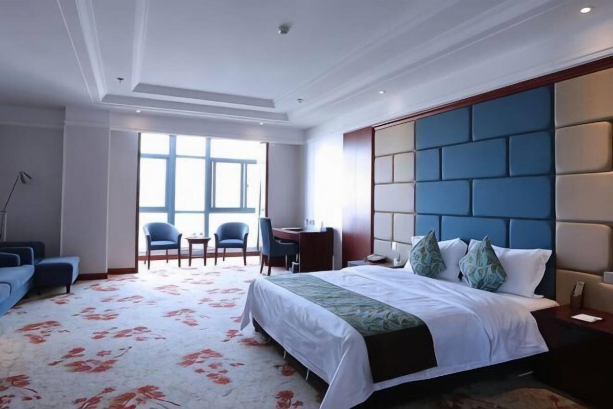 A hotel room with a large bed, a desk, two chairs, and a view of the outdoors.
