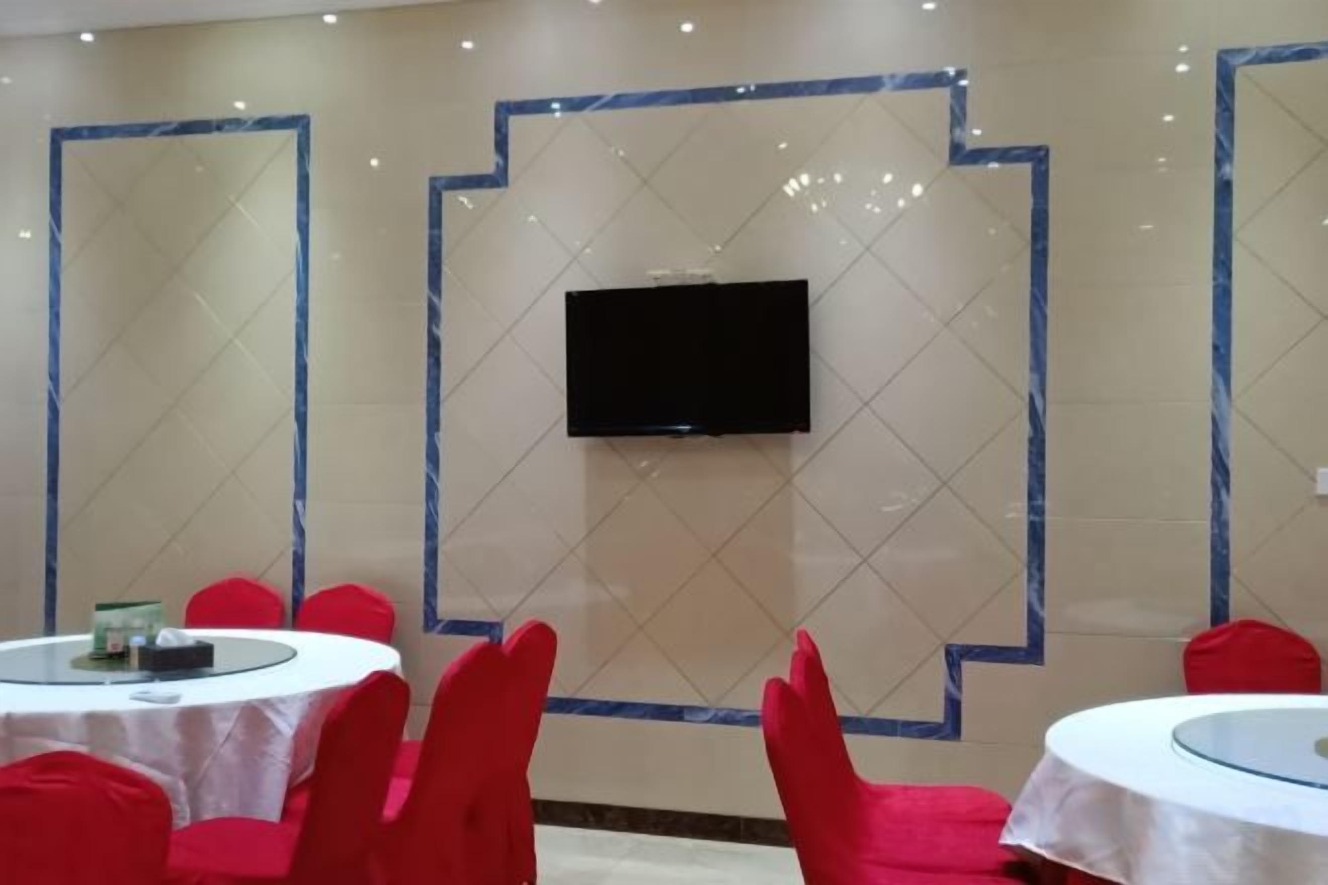 A conference room with a flat-screen TV mounted on the wall, round tables with white tablecloths, and red chairs.
