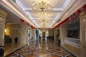 Un vestíbulo de hotel con candelabro, suelo de mármol y faroles rojos.