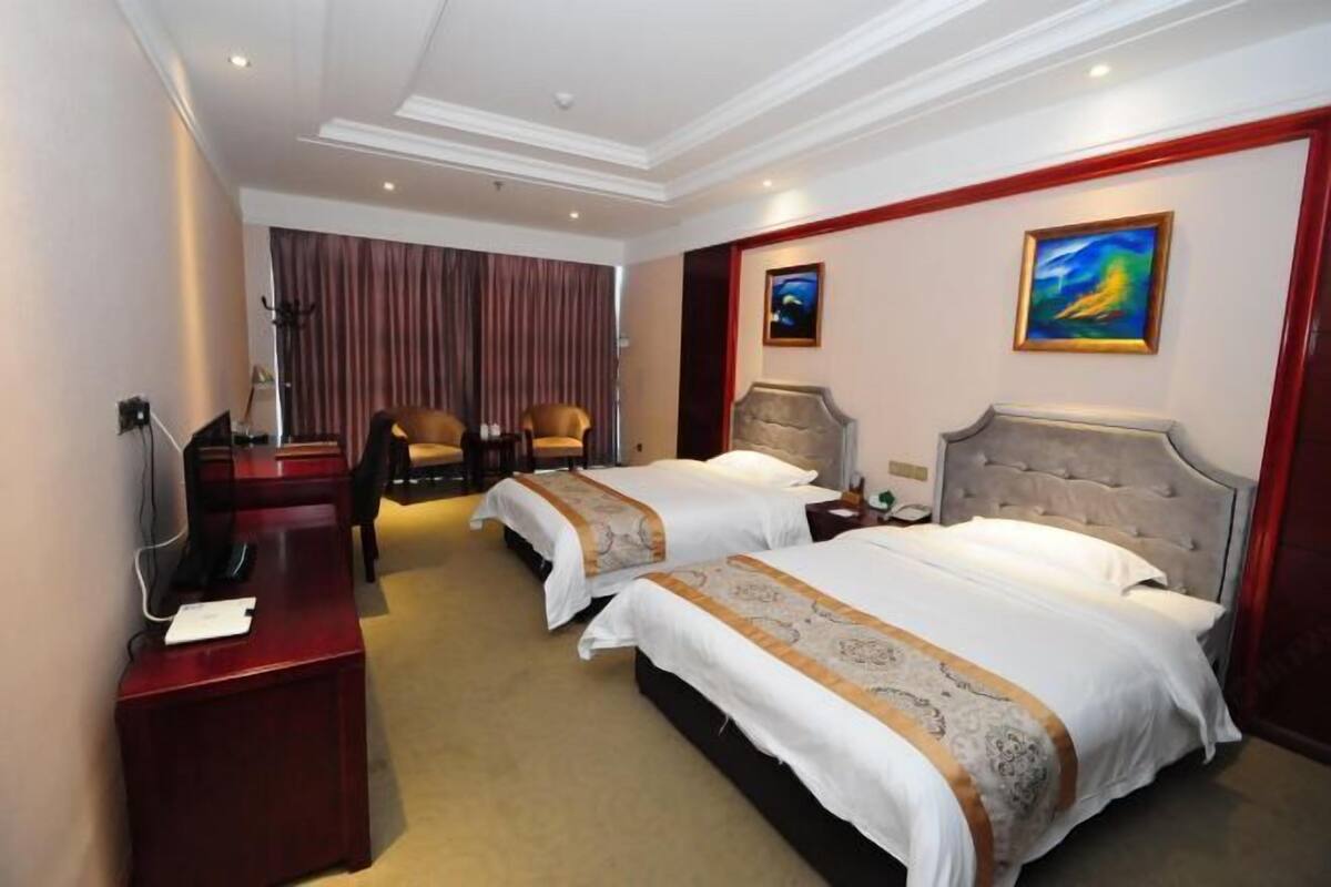 A hotel room with two beds, a desk, a telephone, and a painting on the wall.