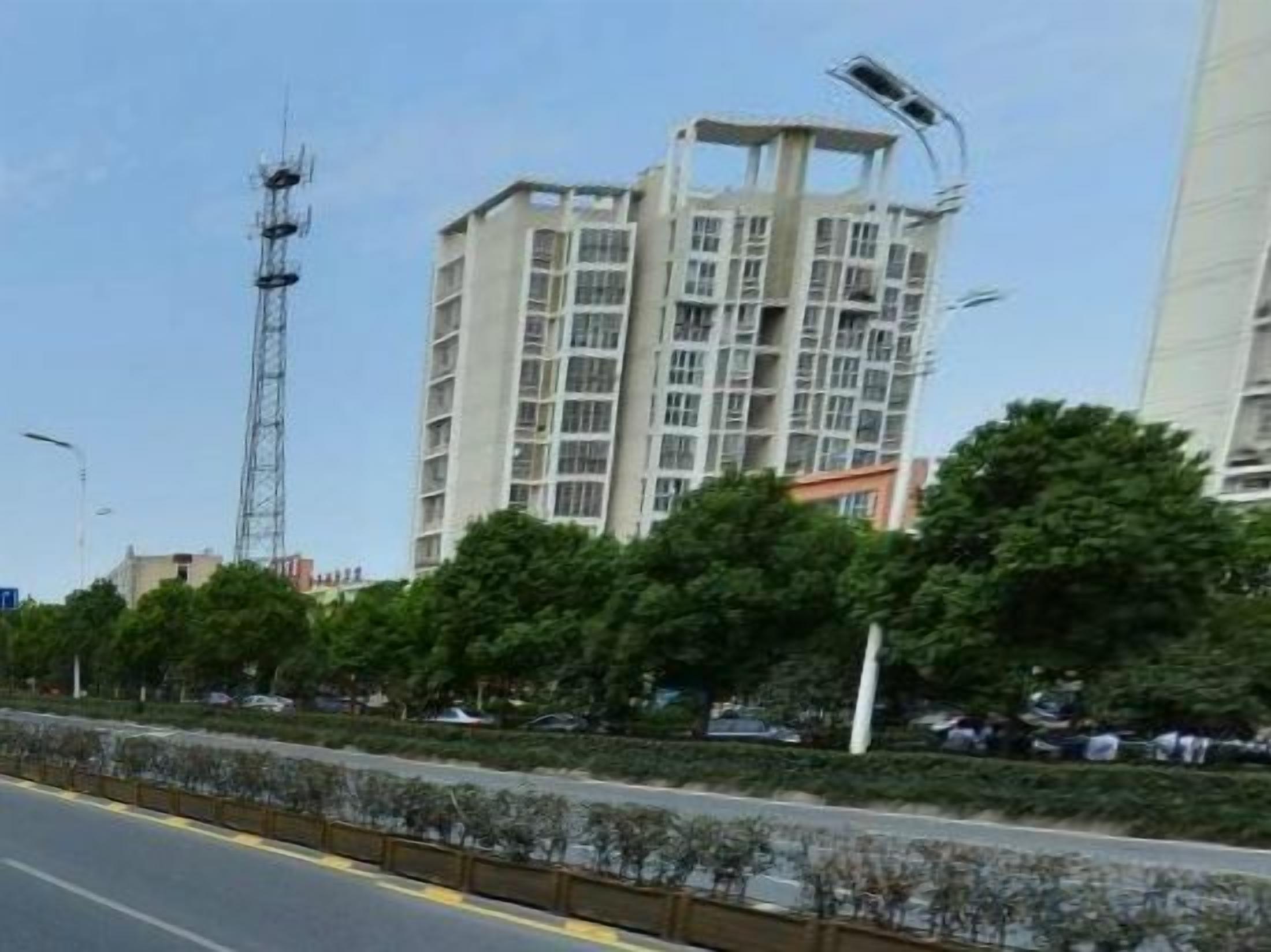 A multi-story building with a modern architectural design, surrounded by greenery and a clear sky.