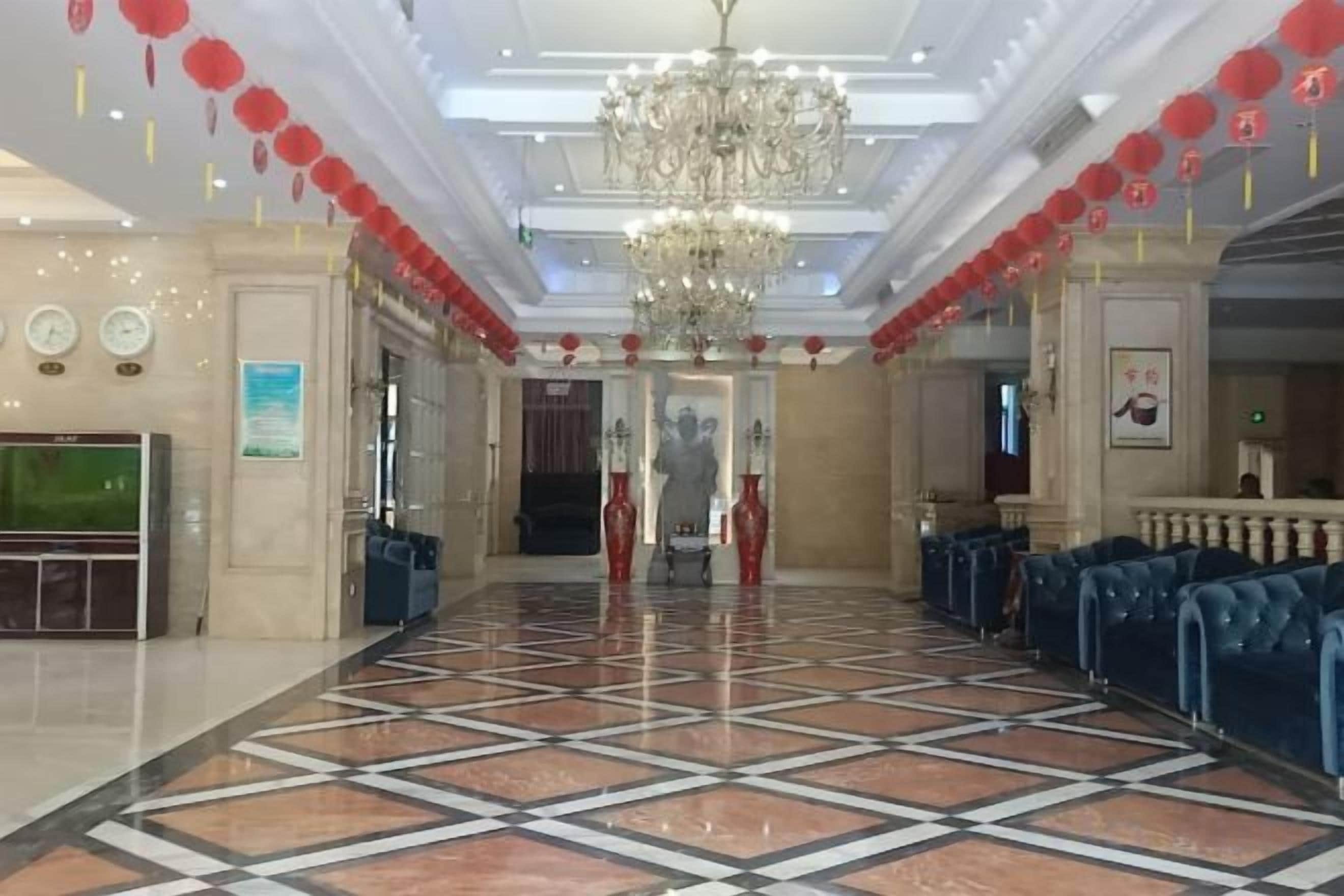 A hotel lobby with a chandelier, red lanterns, a TV, and blue seating.