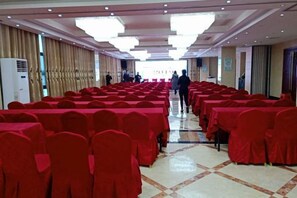 A banquet hall with rows of tables covered in red tablecloths and chairs, a tiled floor, and a long corridor leading to a door. - Hanxiang International Hotel (Feidong)