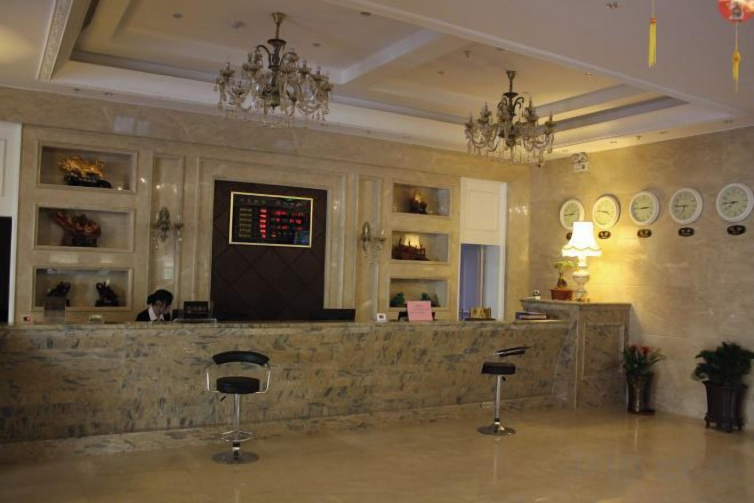 Zona de recepción de hotel con mostrador de mármol, taburetes de bar, candelabro y relojes de pared.