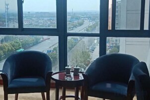 Una habitación con dos sillas y una mesita, ventanas amplias con vistas a una calle y edificios.