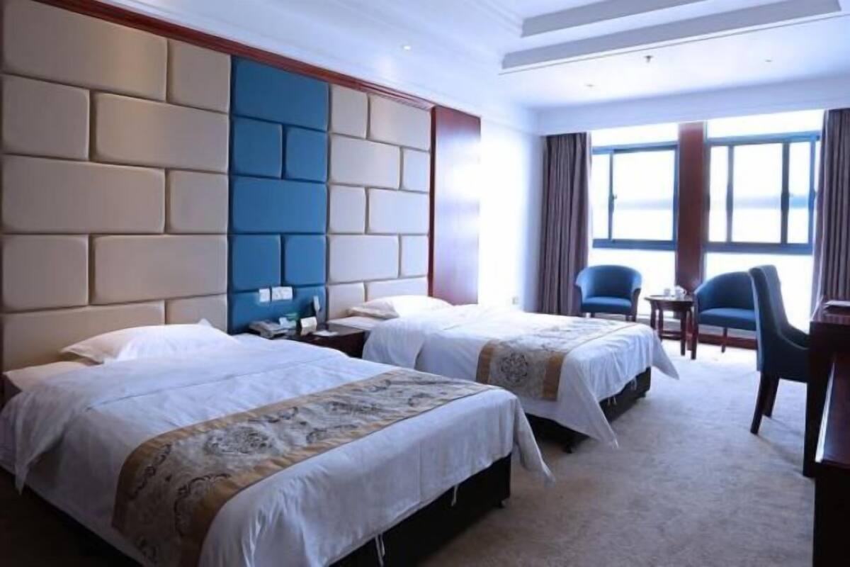 A hotel room with two beds, a large window, a blue chair, and a small table.