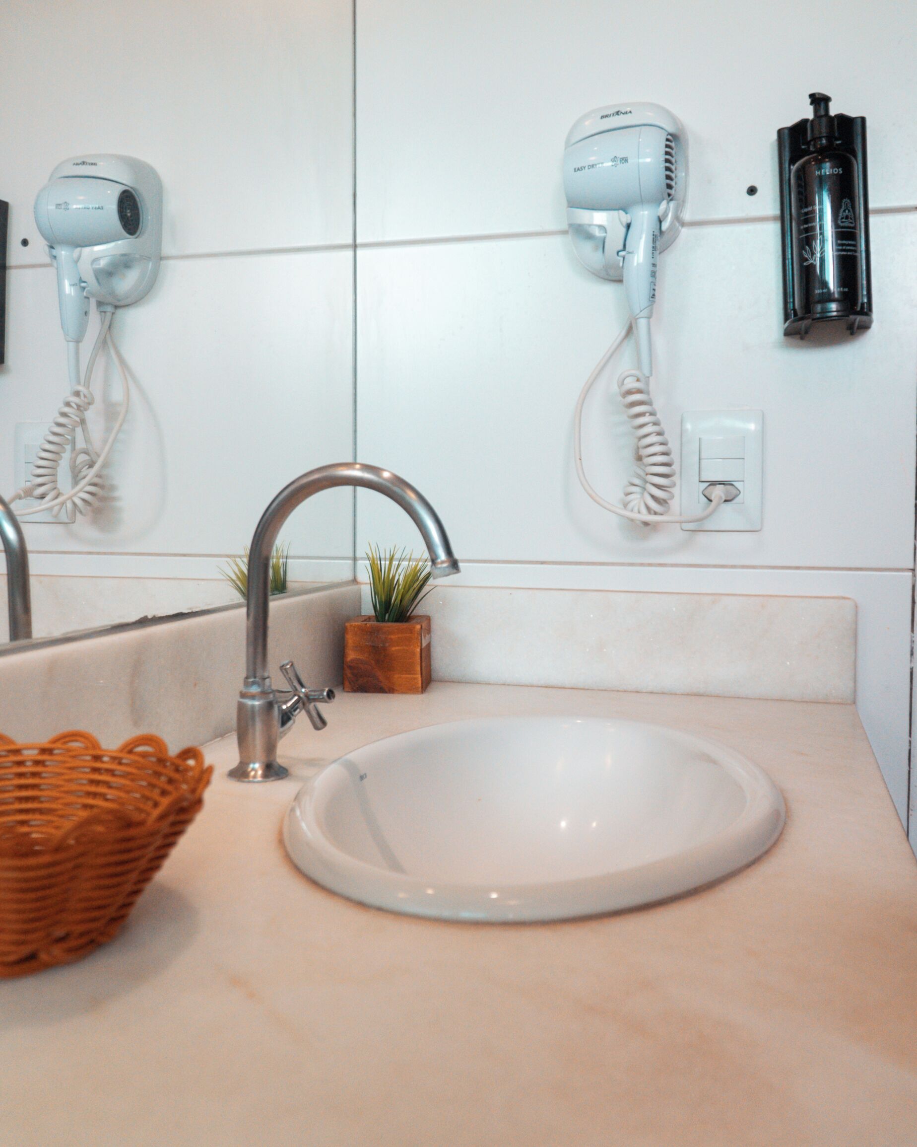 A bathroom with a sink, a mirror, a hairdryer, and a bottle of hair product.