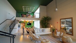 Amplia sala de estar con una escalera, un conjunto de sofás, sillas de mimbre y un espejo grande.
