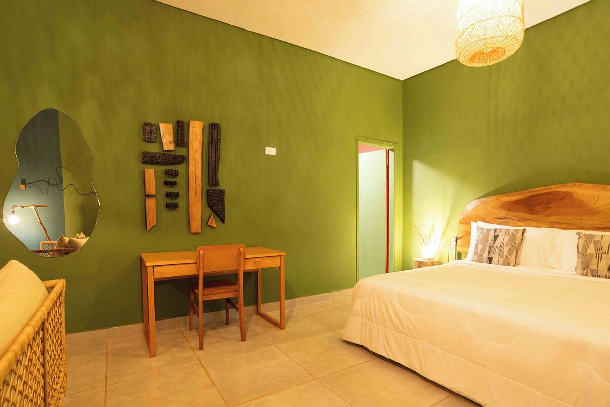 A bedroom with a bed, a desk, a chair, a mirror, and a wall with decorative items.