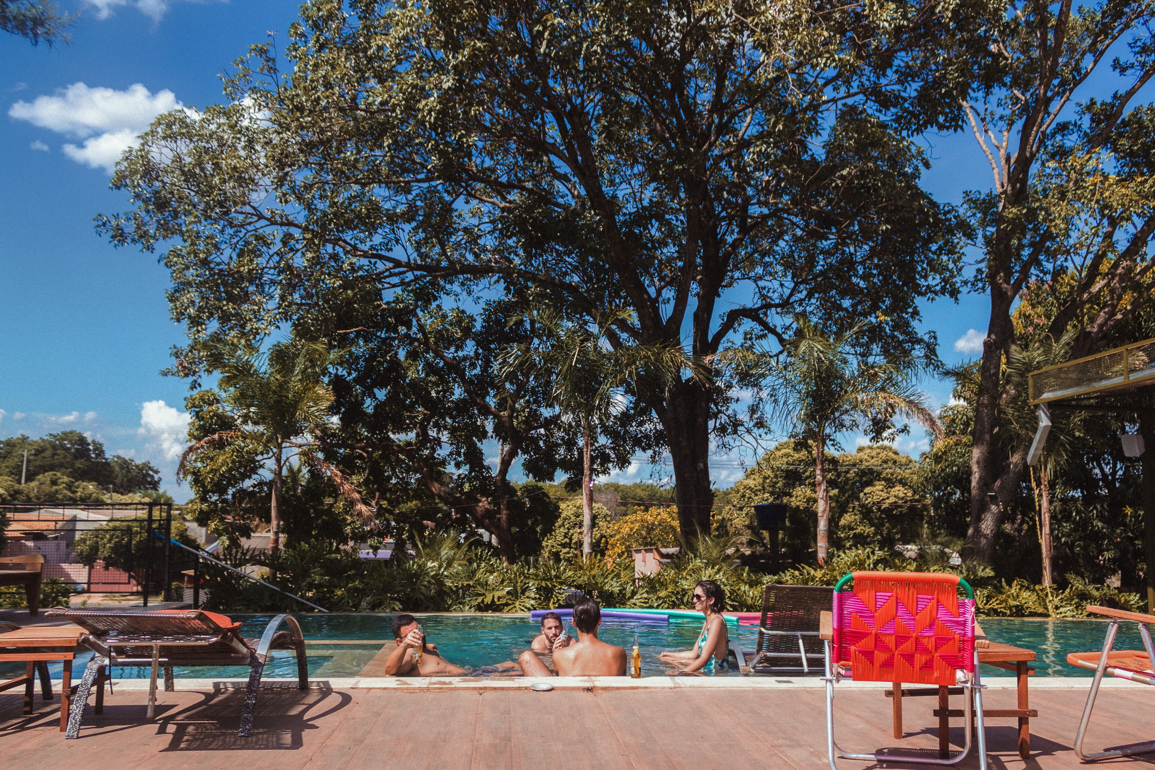 A poolside area with lounge chairs and a table, surrounded by trees and a clear sky.