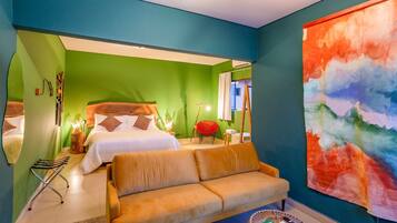 A hotel room with green walls, a large abstract painting, a sofa, a bed with white linens, and a red chair.