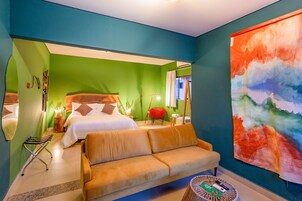 Habitación de hotel con paredes verdes, un cuadro abstracto grande, un sofá, una cama con ropa blanca y una silla roja.
