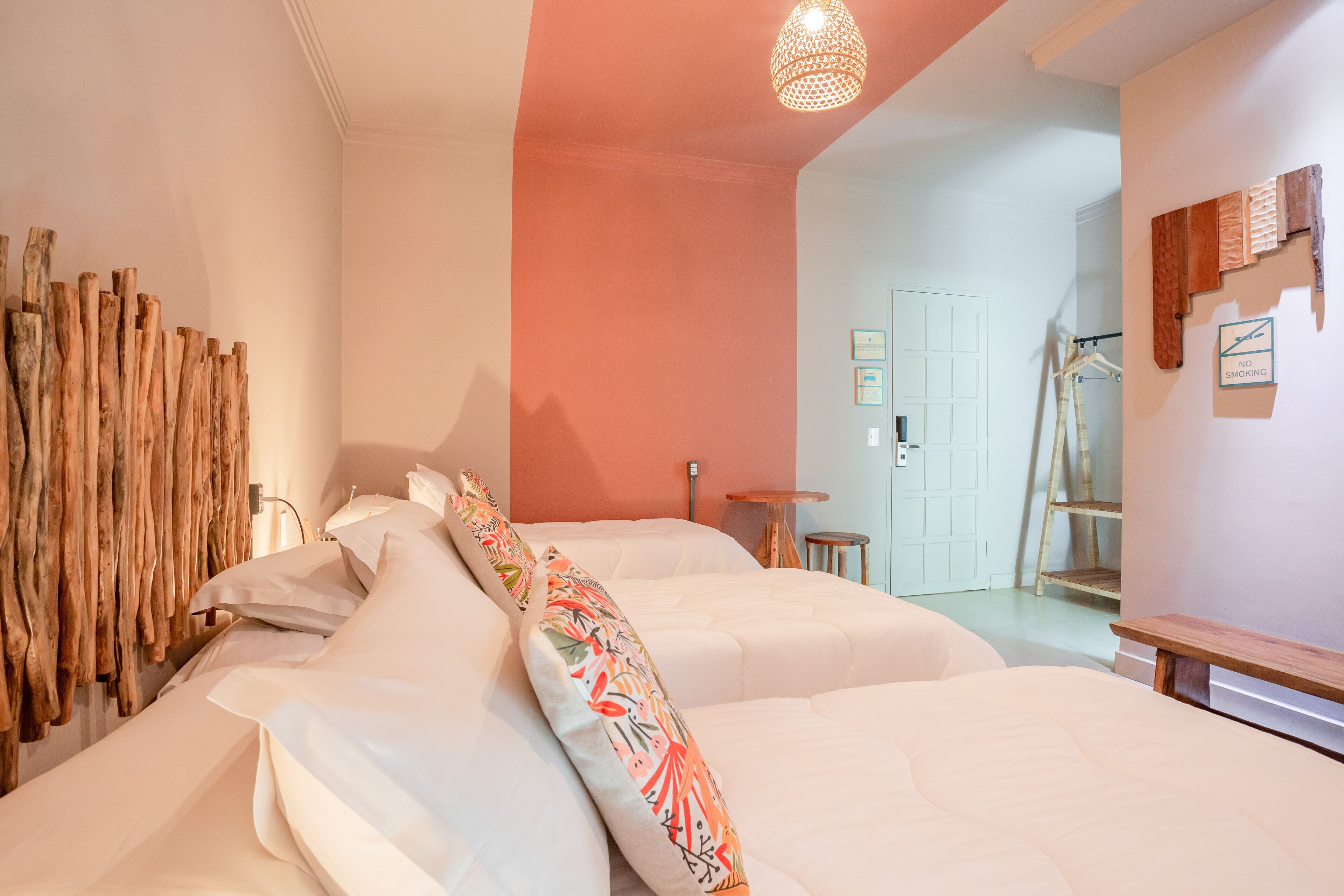 A bedroom with two beds, a wooden wall decoration, a hanging light fixture, and a 'No Smoking' sign.