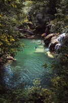 Un cuerpo de agua natural rodeado de densa vegetación, con un puente de madera y afloramientos rocosos.