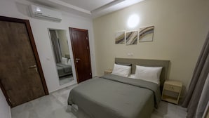 A bedroom with a bed, a nightstand, a dresser, a mirror, and an air conditioning unit. - Le Quartz - Luxury 2 Bed Room Apartments with sea view or overlooking the city (Abidjan)
