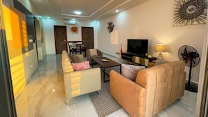 A modern living room with a sofa, a coffee table, a TV, and a fan. - Le Quartz - Luxury 2 Bed Room Apartments with sea view or overlooking the city (Abidjan)