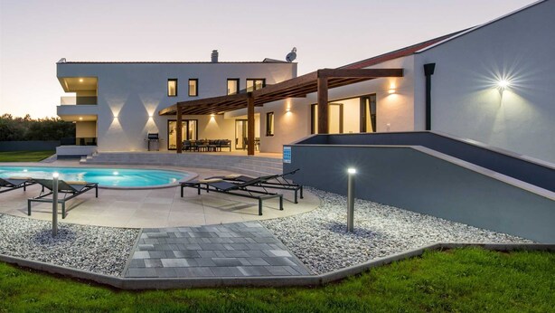 Una casa moderna con piscina, mobiliario exterior y un patio cubierto.