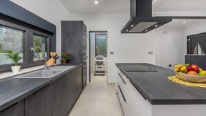 Una cocina moderna con encimeras oscuras, una isla grande y vistas a través de una puerta abierta.