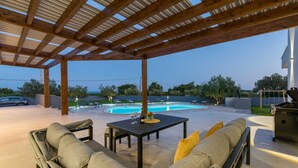 Un patio exterior con piscina, sillones de descanso y una zona de estar cubierta.