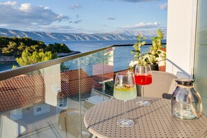 Een balkon met een tafel, twee drankjes, een glazen pot en uitzicht op zee en bergen.